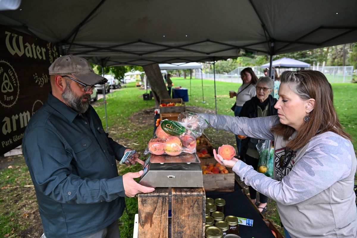 Tina Lohman, right, weighs some of the last peaches of the season from Spring Water Farm on Wednesday at the Spokane Farmers Market in Browne’s Addition’s Coeur d’Alene Park, while farmer James Rowley, left, checks the weight.  (Jesse Tinsley/THE SPOKESMAN-REVIEW)