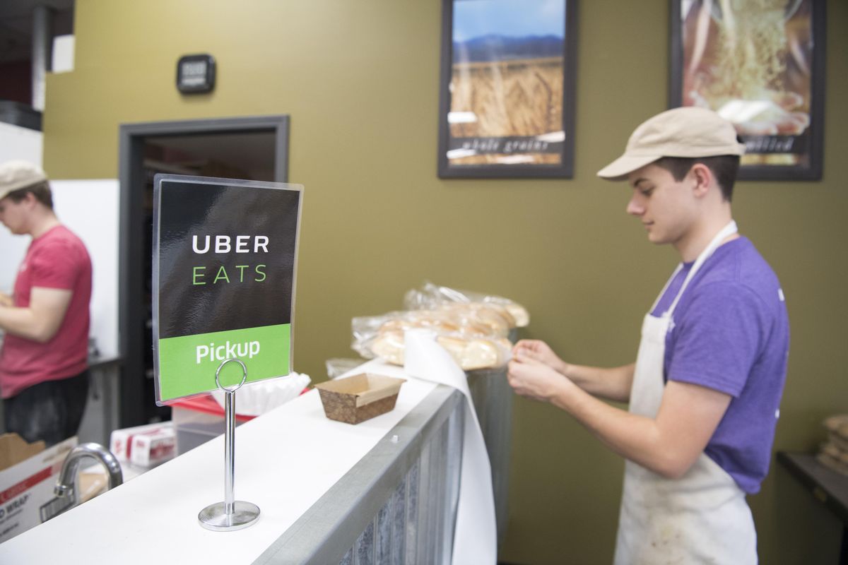 Cole Shirley, right, wraps dinner rolls next to the spot in Great Harvest Bread Co. places the Uber Eats orders that await pickup Tuesday. Great Harvest, on Spokanes South Hill, makes their lunches and bread products available through Uber and other delivery services. (Jesse Tinsley / The Spokesman-Review)