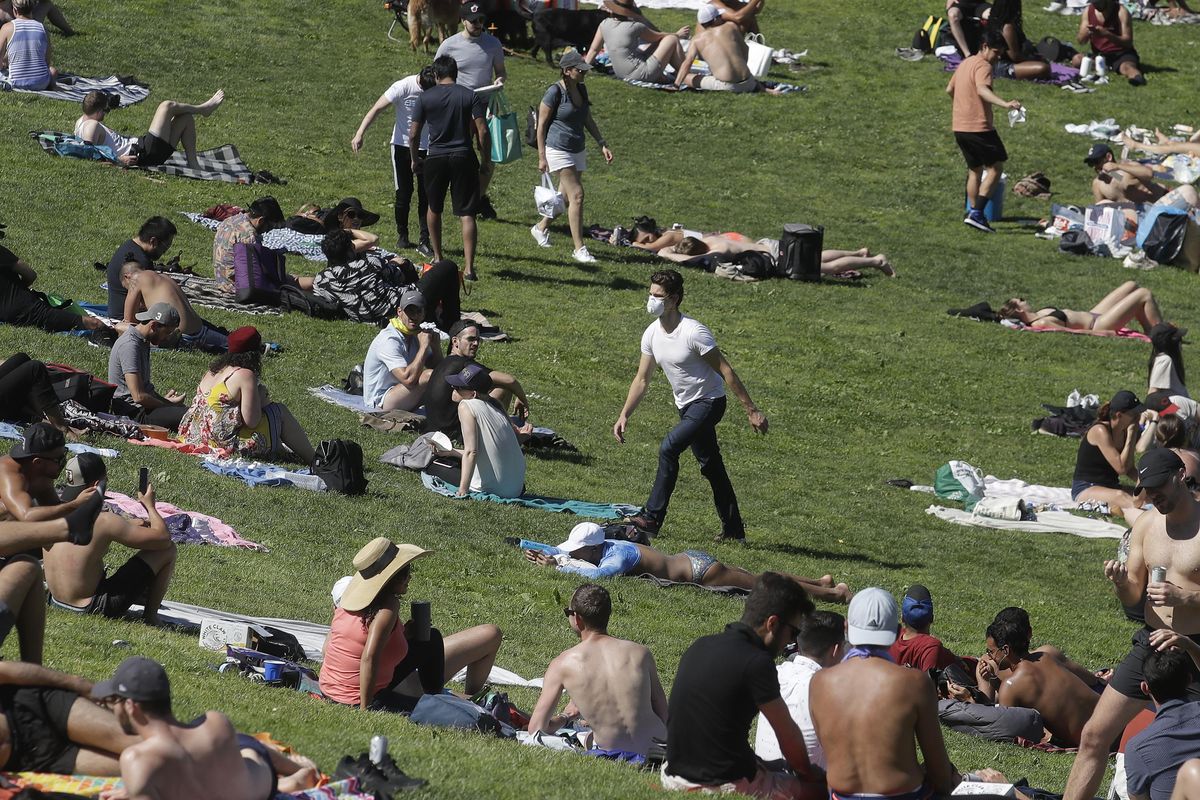 A man wears a face mask while walking through a crowd of visitors at Dolores Park during the coronavirus outbreak, Sunday, May 24, 2020, in San Francisco.A new analysis finds that by early May, 39% of confirmed cases in Washington state were among people age 20 to 39, while those 19 and younger accounted for 11%. (Jeff Chiu / Associated Press)