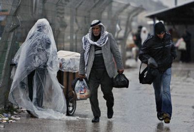 
Palestinian men walk past a vendor covered with plastic wrapping after crossing the Israeli army's Hawara Checkpoint near the West Bank city of Nablus on Tuesday. 
 (Associated Press / The Spokesman-Review)