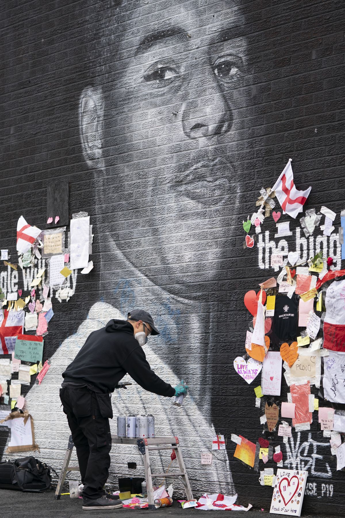 AT LEFT: Street artist Akse P19 repairs the mural of Manchester United striker and England player Marcus Rashford on the wall of the Coffee House Cafe on Copson Street on Tuesday in Withington, Manchester, England. The mural was defaced with graffiti in the wake of England losing the Euro 2020 soccer championship final match to Italy, but subsequently covered with messages of support by well wishers.  (Jon Super)