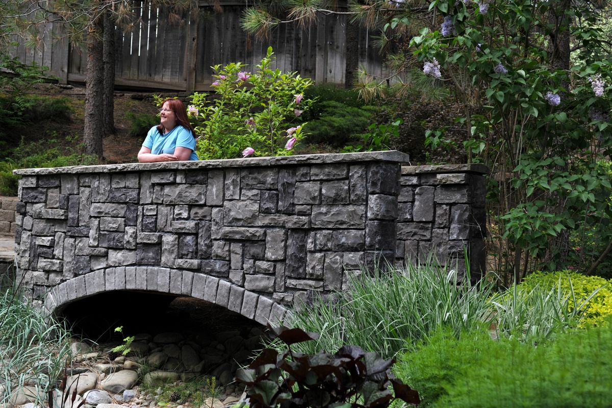 LeAnn Whiting stands on a bridge in her garden at her South Hill home, among those featured on the Spokane in Bloom Garden Tour. (Tyler Tjomsland)