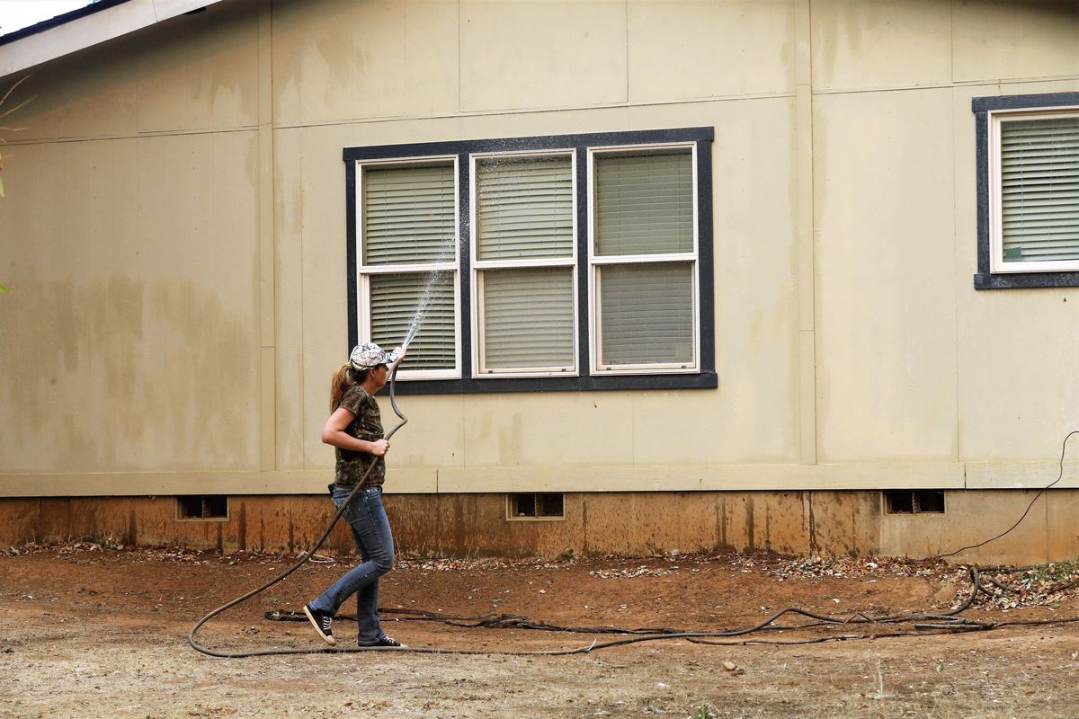 Katie Wright hoses down a family home on Casa Drive in an evacuated neighborhood about a half-mile from the Fawn Fire near Redding, Calif., on Thursday, Sept. 23, 2021. Evacuations have been ordered in a Northern California community as a new wildfire spreads.  (Mike Chapman)