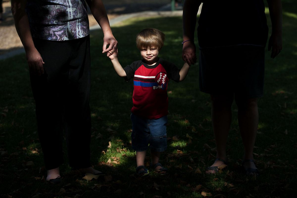 Two-year-old William Trotz holds hands with his adoptive mother, Michelle Trotz, left, and his biological mother, Diana Stegner, during a visit to Mission Park in Spokane on Sept. 22. Trotz believes it’s important for William to know his biological mother. (Kathy Plonka)