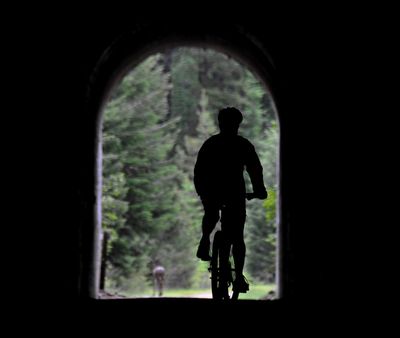 A bicyclist follows a mule deer out of Tunnel 22 on the Route of the Hiawatha rail trail near Lookout Pass. (Rich Landers)