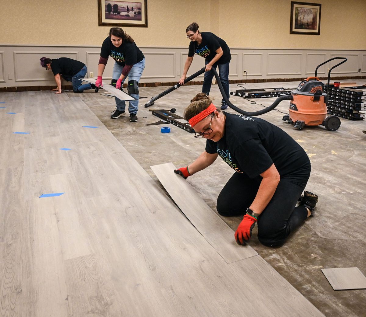 Employee representing 18 local credit unions, including Becky Gaines, STCU, standing, Sarah Dahmen, Spokane Media Federal Credit Union, vacuuming and Wendie Ellis, Horizon Credit Union, front, join forces to lay flooring inside Spokane