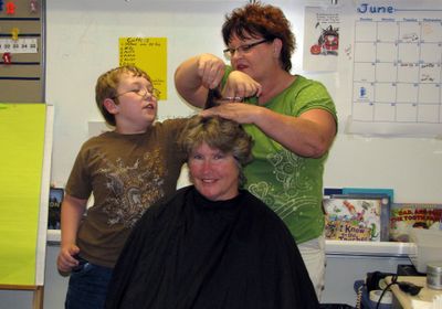 Teacher Kay Wright’s longtime hair stylist, Eileen Moffitt, helps student Stetson Plummer with the first cut. Of all Wright’s students, Stetson read the most, reaching almost 6,000 minutes, so he got to take the first cut. Photo by Jody Edwards (Photo by Jody Edwards / The Spokesman-Review)