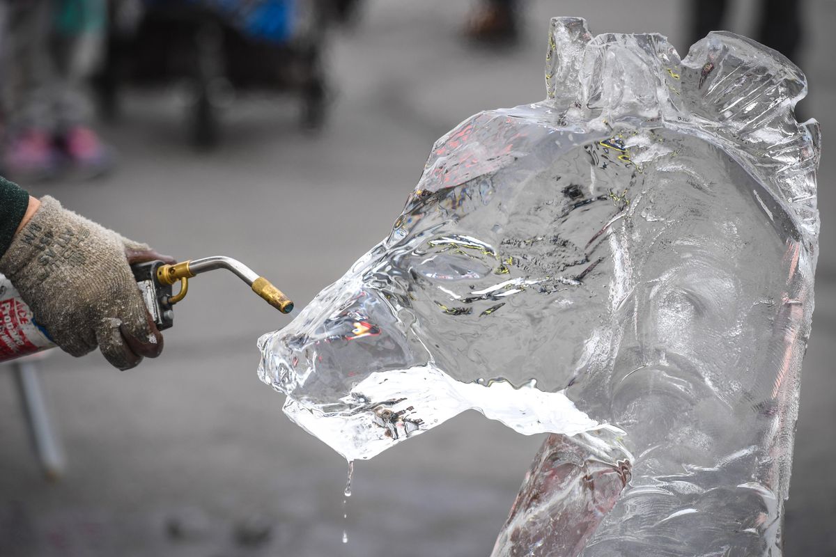 Trevor Jensen uses a torch to shape a chess knight piece during ice carving at the Holiday on the Ave celebration, Saturday, Dec. 14, 2019, in the Sprague Union District. (Dan Pelle / The Spokesman-Review)