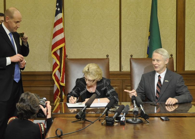 OLYMPIA -- Gov. Chris Gregoire signs the election results certifying Referendum 74, the same-sex marriage law, as Secretary of State Sam Reed looks on and communications director Cory Curtis, at left, holds a handful of pens from the signing. (Jim Camden)