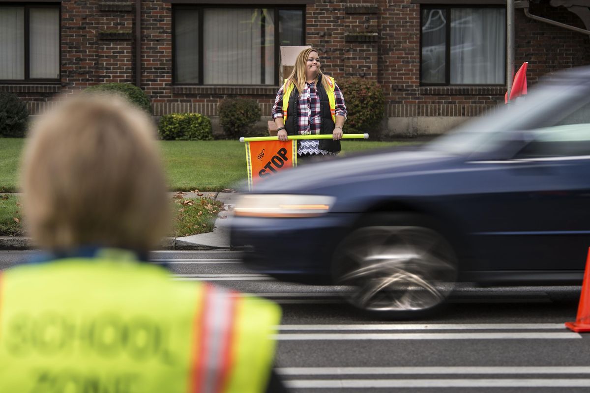 Finch Elementary School crossing guards, Tomi Wheller, center, and Sandy Smith, left, watch traffic along Northwest Boulevard slow to 20 mph during the morning commute, Oct. 6, 2016, in Spokane Wash. The cars traveling east (shown) are subject to fines for speeding if caught by the school-zone camera. (Dan Pelle / The Spokesman-Review)