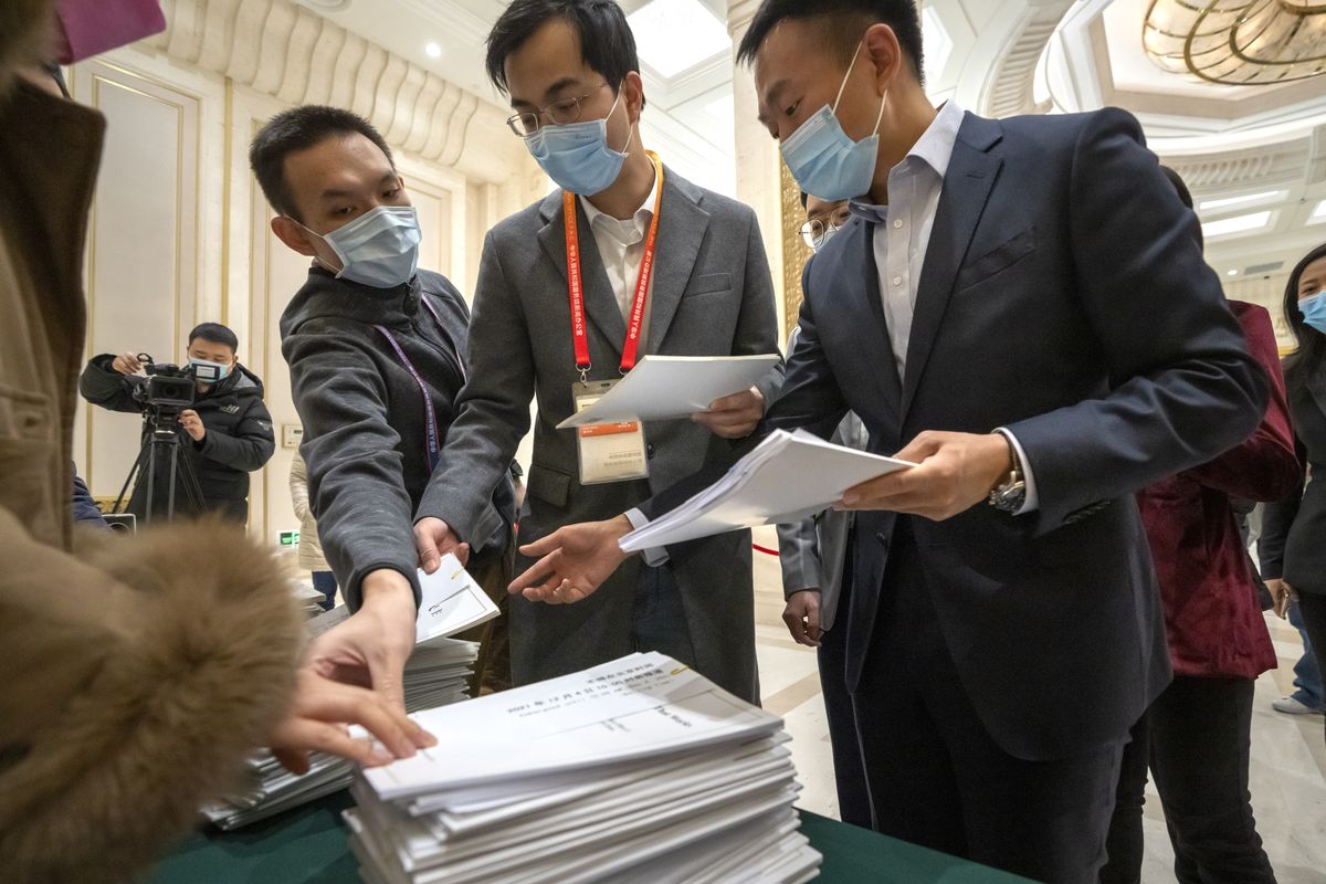 Journalists reach for copies of a Chinese government-produced report titled "Democracy that Works" before a press conference at the State Council Information Office in Beijing, Saturday, Dec. 4, 2021. China's Communist Party took American democracy to task on Saturday, sharply criticizing a global democracy summit being hosted by President Joe Biden next week and extolling the virtues of its governing system.  (Mark Schiefelbein)