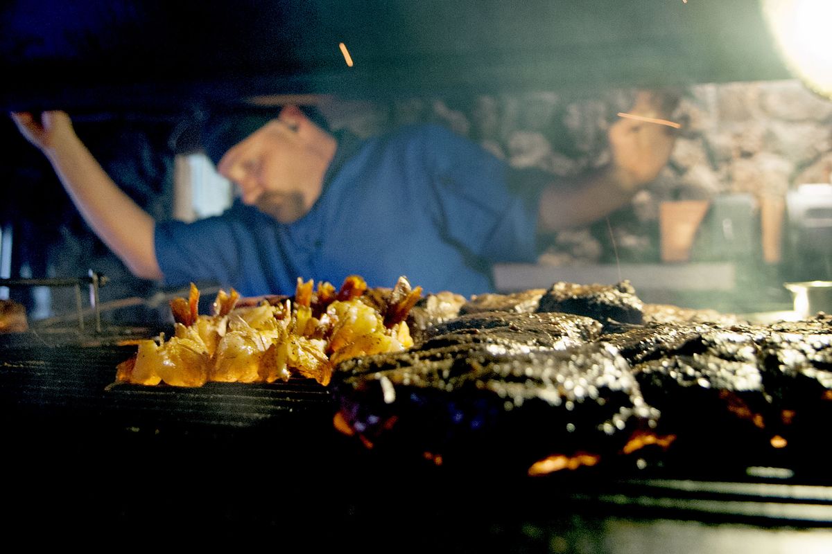 Wolf Lodge Inn head cook Cory Parker keeps an eye on the wood-grilled tiger shrimp and steaks on the fire pit at the iconic restaurant east of Coeur d’Alene. (Kathy Plonka)