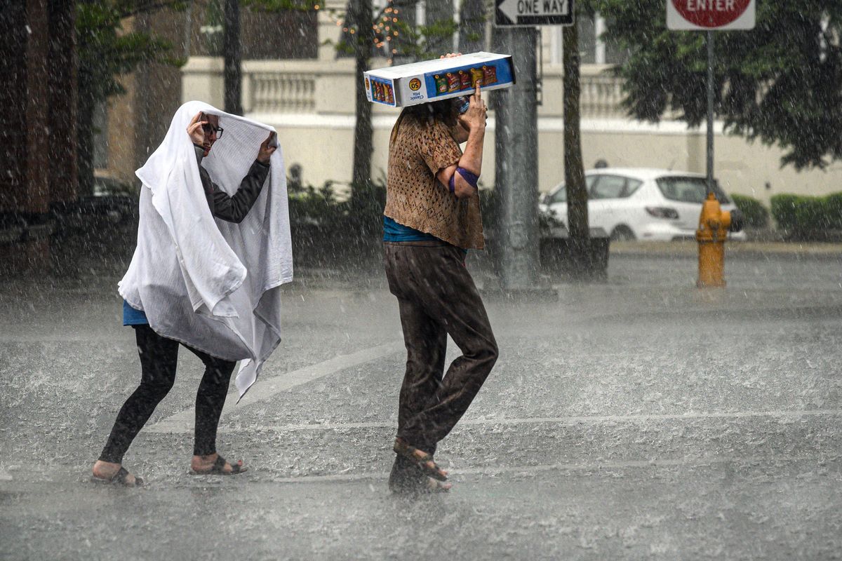 Crossing Riverside Avenue, Jorie Jenkins, left, and a pedestrian use every means necessary to shield themselves from a torrential downpour that flooded street across the city of Spokane, Thursday, May 16, 2019. (Colin Mulvany / The Spokesman-Review)