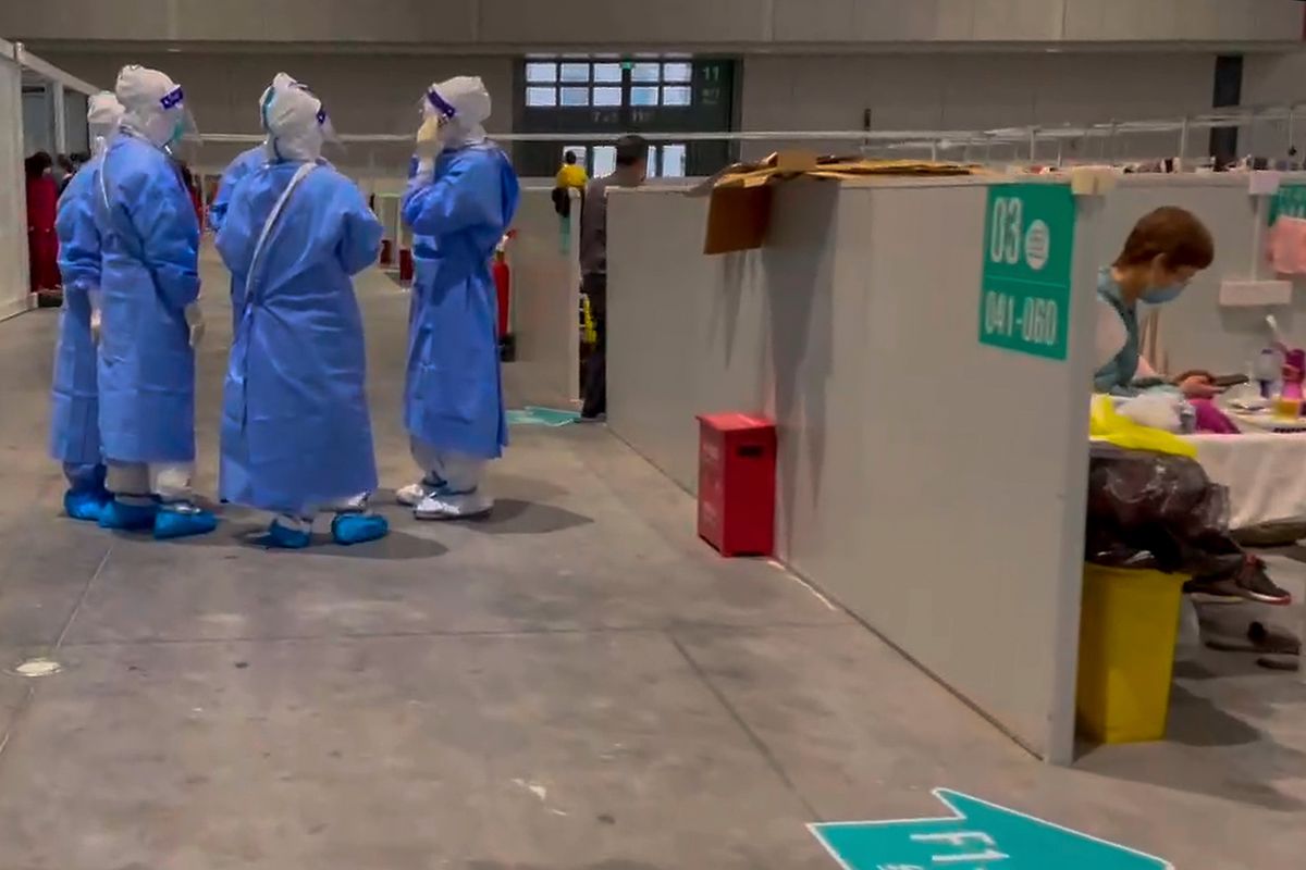 In this image taken from video provided by Beibei, who asked to be identified only by her given name, medical workers wearing protective suits chat as a resident takes a rest at the National Exhibition and Convention Center on April 15, 2022, in Shanghai. The convention center converted to a quarantine facility set up for people who tested positive but have few or no symptoms.  (Beibei)