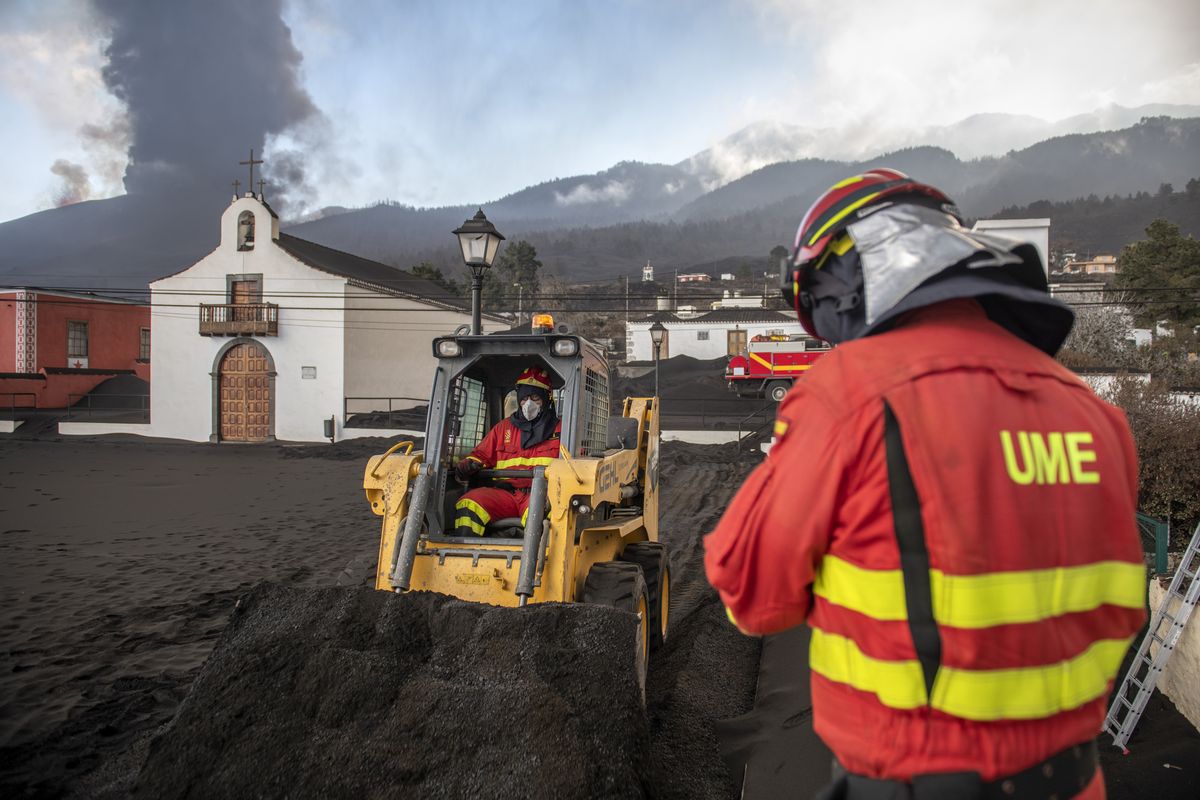 Military Emergency Unit personal clear black ash from volcano as it continues to erupt lava behind a church on the Canary island of La Palma, Spain on Wednesday Oct. 13, 2021. A new lava stream from an erupting volcano threatened to engulf another neighborhood on its way toward the Atlantic Ocean. Island authorities have ordered the evacuation of around 800 people from a section of the coastal town on Tuesday after the lava took a new course and put their homes in its probable path of destruction. (Saul Santos)