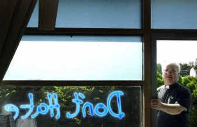 
The Rev. Eugene Tracy stands next to words painted on St. Charles Catholic Church. 