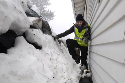 Avista meter reader Rachel Rushing struggles her way to a gas meter buried in snow between a pickup truck and a house on the 3800 block of south Hatch Road in Spokane on Thursday. She was unable to view the dials on the meter.  (Dan Pelle / The Spokesman-Review)