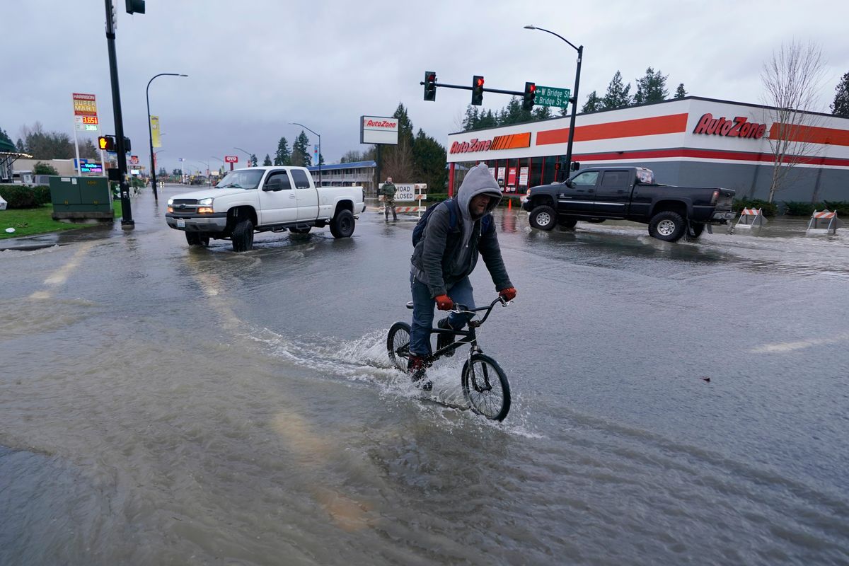 A cyclist rides on a flooded street near Interstate 5, Friday, Jan. 7, 2022, in Centralia, Wash. Snow and rain forced the closure of parts of Washington state