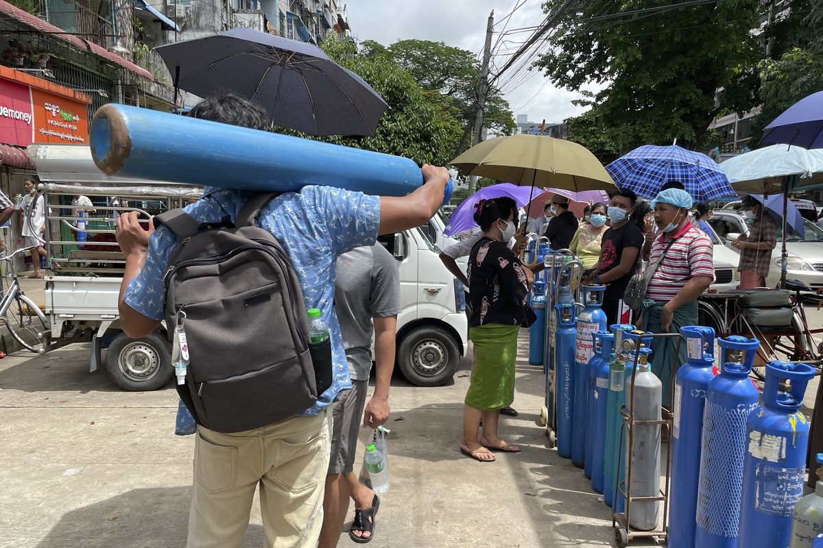 A man carries an oxygen tank while others line up with their oxygen tanks outside an oxygen refill station in Pazundaung township in Yangon, Myanmar, Sunday, July 11, 2021. Myanmar is facing a rapid rise in COVID-19 patients and a shortage of oxygen supplies just as the country is consumed by a bitter and violent political struggle since the military seized power in February. (STF)