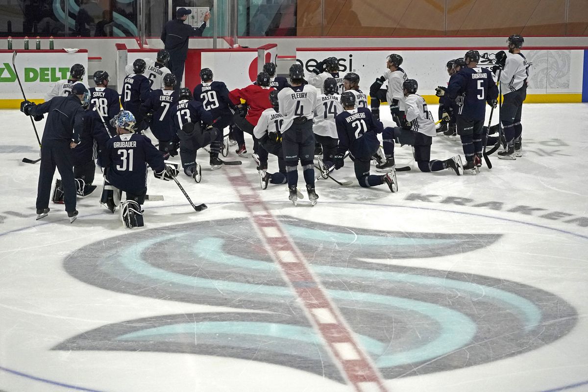 Seattle Kraken players kneel on the ice at their training facility as head coach Dave Hakstol outlines a play during NHL hockey practice, Thursday, Oct. 21, 2021, in Seattle. The Kraken will face the Vancouver Canucks, Saturday in Seattle for the expansion team