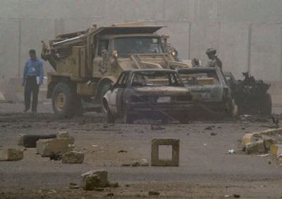 
A U.S. soldier directs a truck to clear away burned cars left after an attack by a man wearing a belt of explosives and a suicide car bomber near a police station in central Baghdad, wounding at least nine Thursday. 
 (Associated Press / The Spokesman-Review)