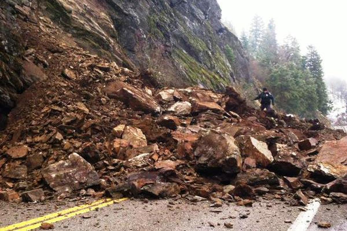 A police officer examines a rock slide that buried Idaho Highway 97 this morning in Beauty Bay along Lake Coeur d
