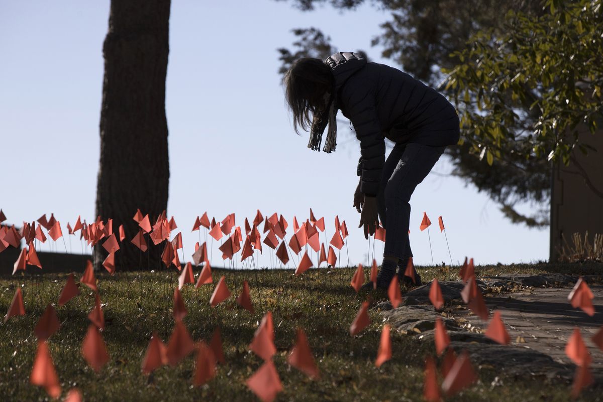 FILE - In this Feb. 10, 2021, file photo, Cindy Pollock does maintenance on the construction flags in her front yard in Boise, Idaho. Pollock began planting the tiny flags across her yard, one for each of the more than 1,800 Idahoans then killed by COVID-19, the toll was mostly a number. Idaho hospital facilities and public health agencies are scrambling to add capacity however they can as the number of coronavirus cases continue to rise statewide. On Thursday, Aug. 26, 2021, some Idaho hospitals only narrowly avoided enacting "crisis standards of care," where scarce healthcare resources are allotted to the patients most likely to benefit, thanks in part to statewide coordination.  (Otto Kitsinger)