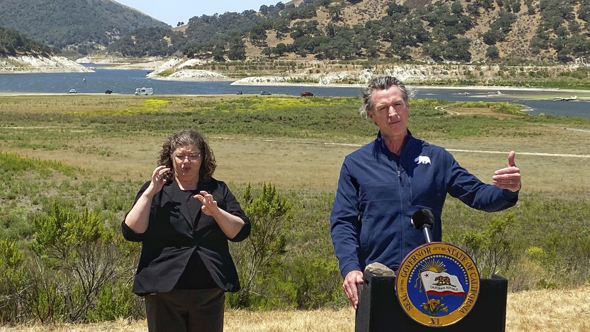 Gov. Gavin Newsom and interpreter Julia Townsend stand at the edge of a diminished Lopez Lake near Arroyo Grande, Calif., Thursday. (David Middlecamp)