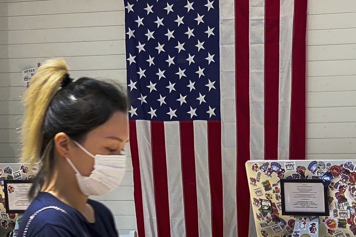 A woman wearing a face mask walks by a counter displaying an American flag at a fashion boutique in Beijing, Sunday, July 11, 2021. China on Sunday said it will take "necessary measures" to respond to the U.S. blacklisting of Chinese companies over their alleged role in abuses of Uyghur people and other Muslim ethnic minorities.  (Andy Wong)