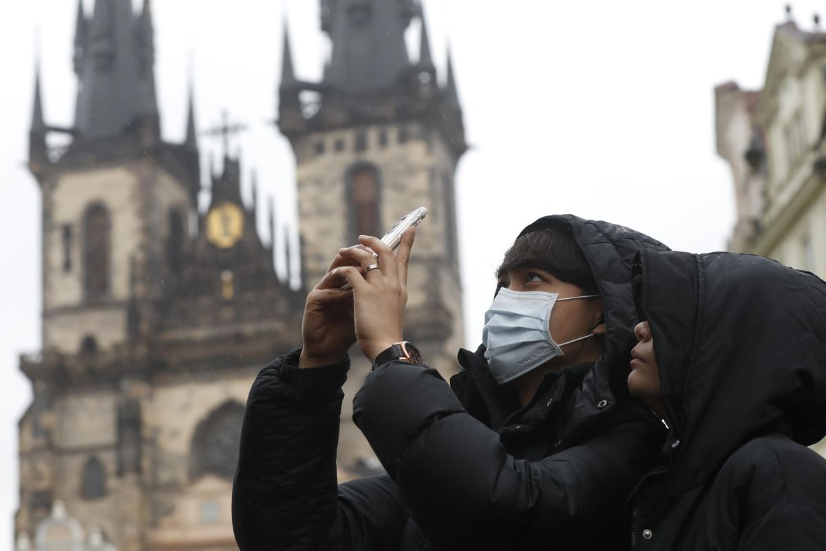 A man wearing a face mask takes a photo at the Old Town Square in Prague, Czech Republic, on March 11. For most people, the new coronavirus causes only mild or moderate symptoms such as fever and cough. For some, especially older adults and people with existing health problems, it can cause more severe illness, including pneumonia. And doctors are now discussing the importance of not touching your face to stop the spread of germs and particles. (Petr David Josek / AP)