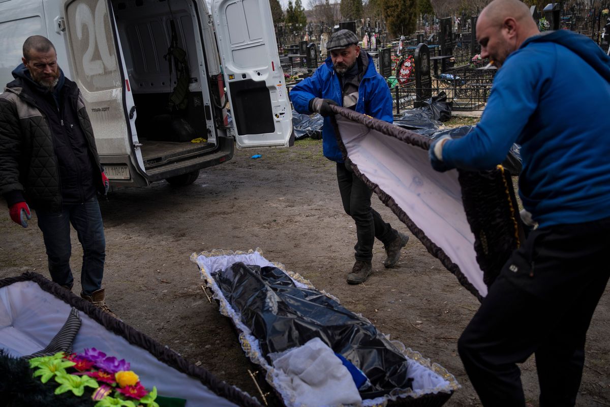Cemetery workers prepare the coffin for a person killed during the war with Russia, as dozens of black bags containing more bodies of victims are seen strewn across the graveyard in the cemetery in Bucha, in the outskirts of Kyiv, Ukraine, Monday, April 11, 2022.  (Rodrigo Abd)