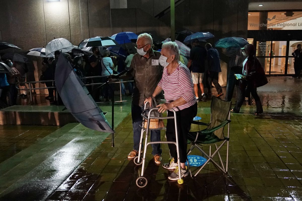 A couple stands in line as rain falls on voters waiting for the precinct to open, Monday, Oct. 19, 2020 in Miami. Florida begins in-person early voting in much of the state Monday. With its 29 electoral votes, Florida is crucial to both candidates in order to win the White House.  (Lynne Sladky)
