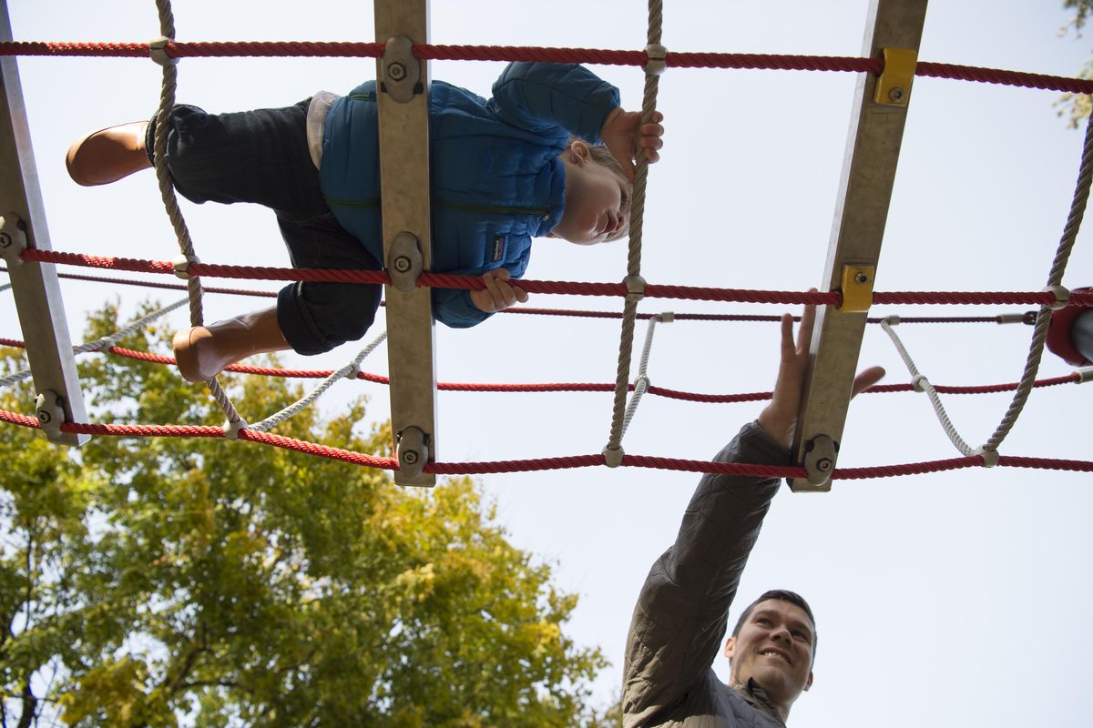Tommy Tribbett, below, encourages his 20-month-old son Boone, to keep crossing the rope bridge on the playground at Manito Park Tuesday, Oct. 17, 2017. The park is one way to keep your kids active as the weather gets colder and the days get shorter. (Jesse Tinsley / The Spokesman-Review)