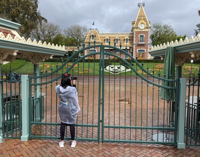 A visitor at Disneyland Resort takes a picture through a locked gate on March 16, 2020. California’s world-famous theme park reopened Friday.  (Associated Press)