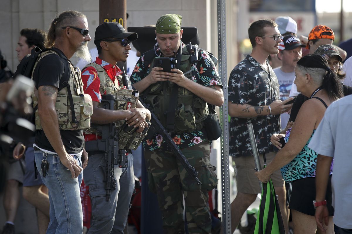 FILE - In this June 20, 2020 file photo, gun-carrying men wearing Hawaiian print shirts associated with the boogaloo movement watch a demonstration near where President Trump had a campaign rally in Tulsa, Okla. People following the anti-government boogaloo movement, which promotes violence and a second U.S. civil war, have been showing up at protests across the nation armed and wearing tactical gear. But the movement has also adopted an unlikely public and online symbol: Hawaiian print shirts.  (Charlie Riedel)