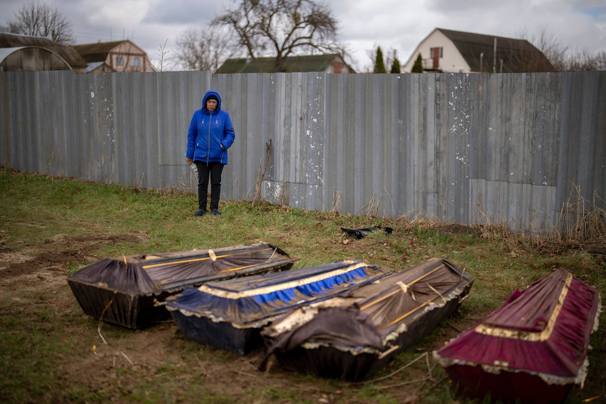 Ira Slepchenko, 54, stands next to coffins, one of them with the body of her husband Sasha Nedolezhko, 43, during an exhumation of a mass grave in Mykulychi, Ukraine on Sunday, April 17, 2022. All four bodies in the village grave were killed on the same street, on the same day. Their temporary caskets were together in a grave. On Sunday, two weeks after the soldiers disappeared, volunteers dug them up one by one to be taken to a morgue for investigation.  (Emilio Morenatti)