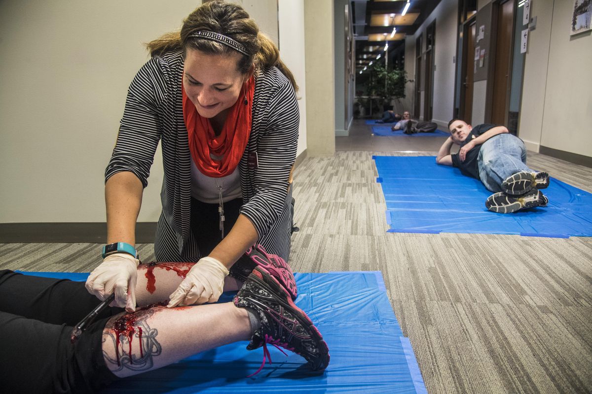Dawn Depriest, clinical professor at the Elson S. Floyd College of Medicine, applies makeup for a bullet wound to a shooting victim as another victim, Rob Carpenter awaits medical help at right, during mass-casualty simulation, Monday, Nov. 13, 2017, at Washington State University College of Nursing. (Dan Pelle / The Spokesman-Review)