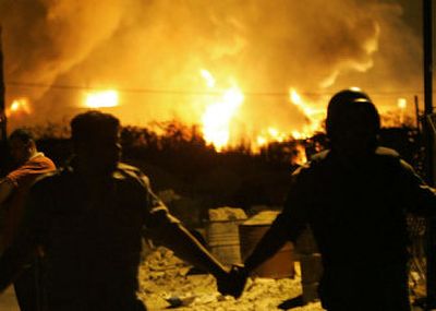 
Lebanese civil defense workers stand in front of fuel storage tanks set ablaze by missiles from  Israeli helicopter gunships at Rafik Hariri International Airport, in Beirut,  late Thursday. 
 (Associated Press / The Spokesman-Review)