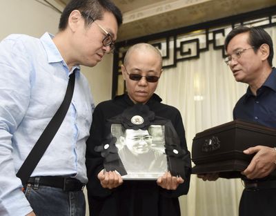 In this Saturday, July 15, 2017, file photo provided by the Shenyang Municipal Information Office, Liu Xia, center, wife of jailed Nobel Peace Prize winner and Chinese dissident Liu Xiaobo, holds a portrait of him during his funeral in Shenyang in northeastern China's Liaoning Province. (Associated Press)