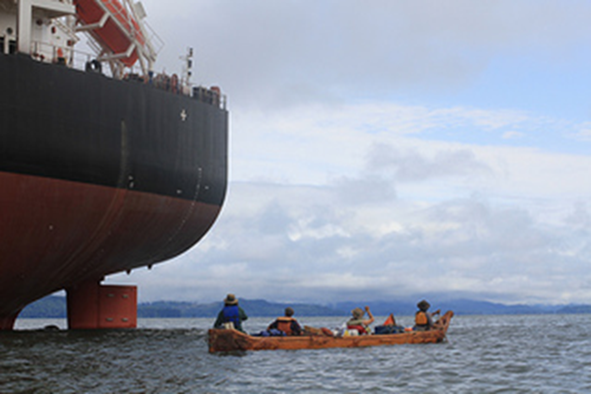 A Sea 2 Source canoe group organized by Voyages of Rediscovery passes by an anchored ship near Astoria, Ore., before beginning their summer 2013 journey up the Columbia River to spotlight the plight of salmon runs that must pass dams en route to spawning grounds. (Voyages of Rediscovery)