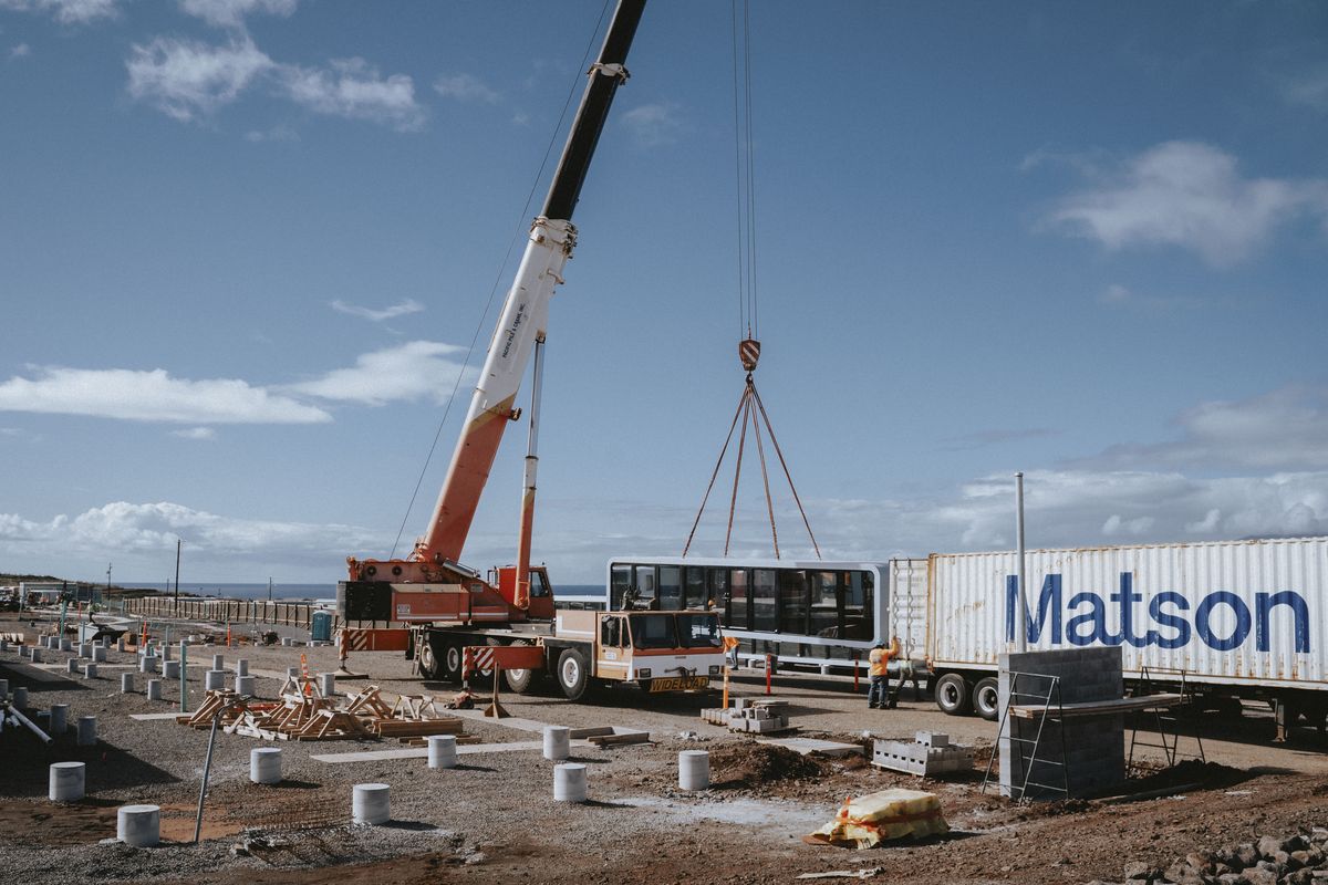 A prefab modular home is lifted out of a container by a crane at a temporary-housing project in Lahaina on Feb. 4.   (Mengshin Lin/For The Washington Post)