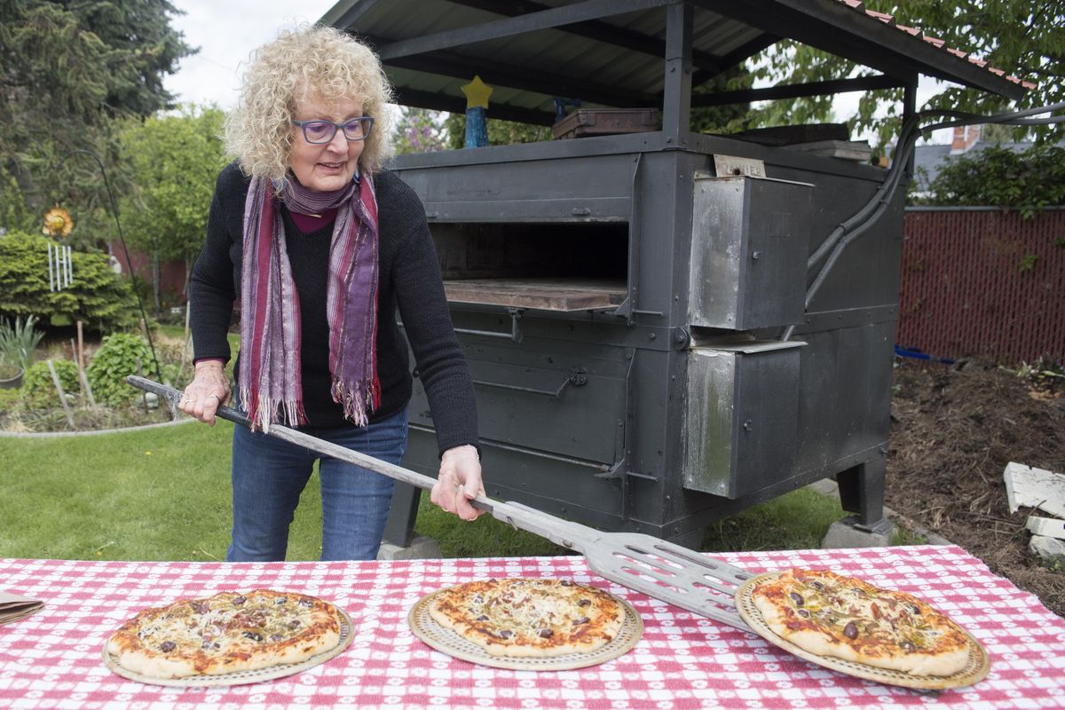 Avid baker Mary Lee Abba-Gaston removes hot pizzas from her commercial bread oven, which sits in her backyard at her North Side home, Monday, May 15, 2017. Abba-Gaston acquired the oven more than 20 years ago from Mount St. Michael, the former Jesuit Scholasticate, and has taught baking classes for many years. She would like to sell the massive, 2-ton oven, into which she’s invested several thousand dollars. But she would drop the asking price of $8,000 if a nonprofit or charity would like to use it. She plans on getting rid of the oven because she plans on selling her house and downsizing. (Jesse Tinsley / The Spokesman-Review)