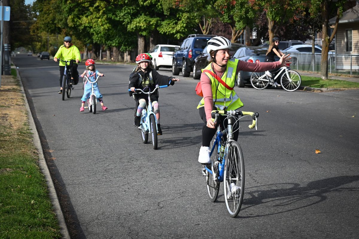 Hailey Coll, right, signals as she leads a group of elementary kids on bikes up to a corner on their way home from Holmes Elementary School in the West Central neighborhood Thursday, Oct. 3, 2024. Taking up the rear of the group is volunteer Tami Linene-Booey at far left. The "bike bus" concept of having adults ride to and from school with children is catching on after River City Youth Ops started a bike bus program at Holmes Elementary.  (Jesse Tinsley/THE SPOKESMAN-REVIEW)