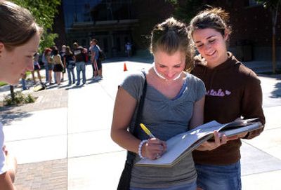 
Shaina Marvel, 15, left, and Brittany Gibson, 15, right, watch as Amy Hallett, 15,  signs a yearbook outside University High School in Spokane Valley on Monday. 
 (Liz Kishimoto / The Spokesman-Review)