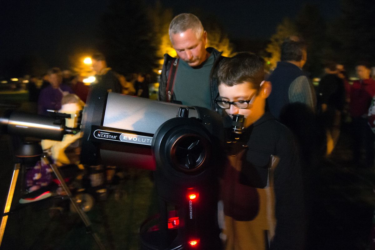 At the Southeast Sports Complex, Isaac Garza, 15, looks at the lunar eclipse through a telescope belonging to Spokane Astronomical Society member Steve Fenick, in back, Sunday evening. The supermoon lunar eclipse drew a large crowd, many with cameras and telescopes. (Colin Mulvany)