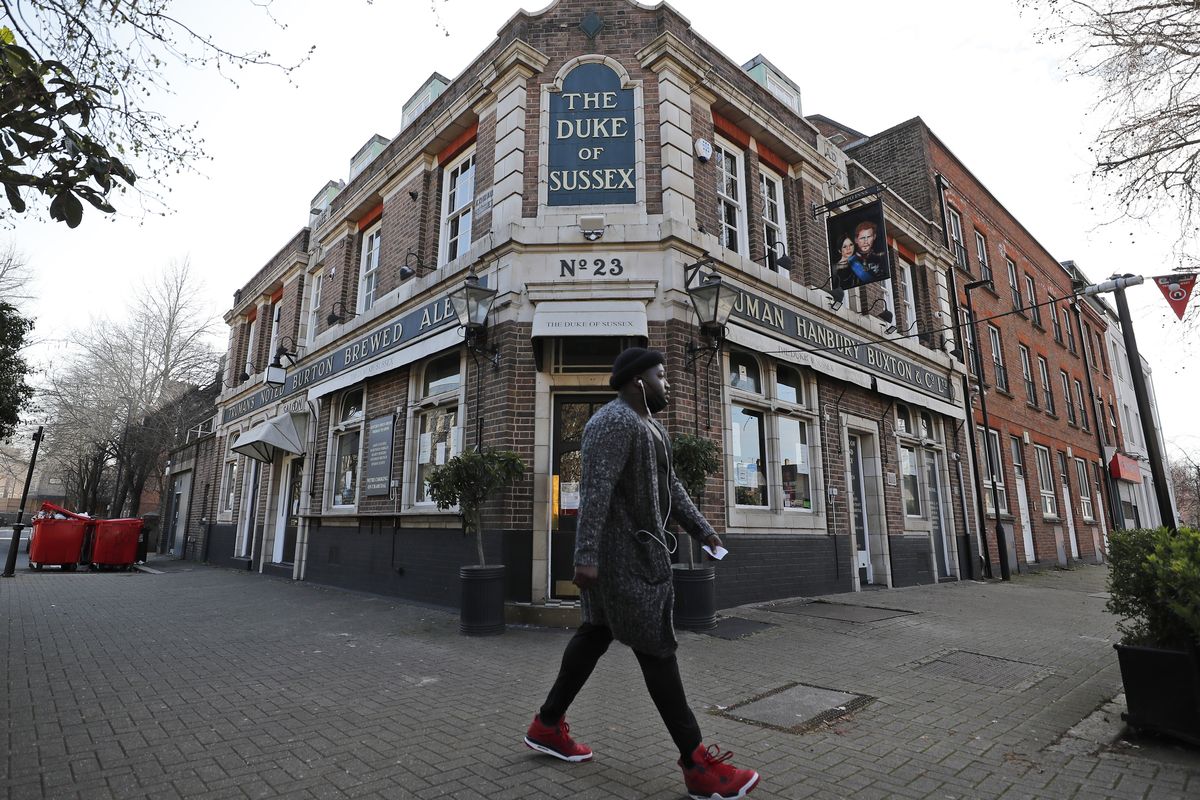 A man walks past the Duke of Sussex pub with a sign depicting the image of Britain