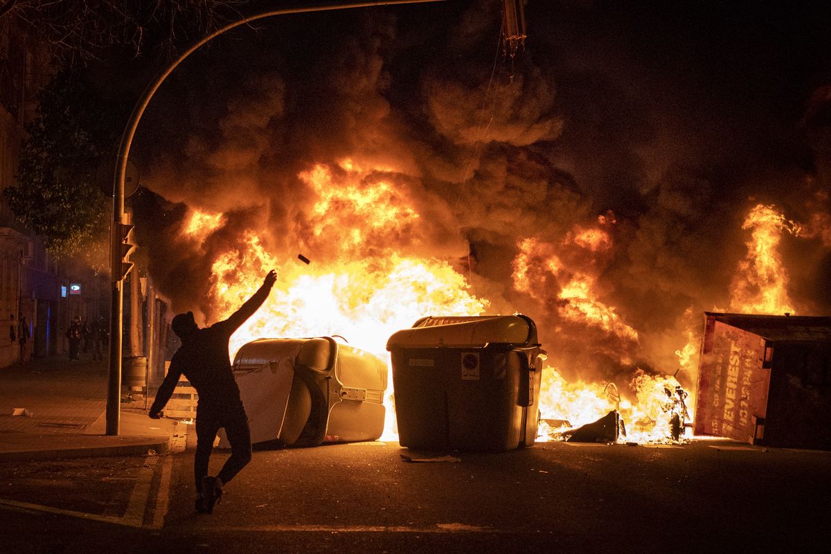 A demonstrator throws a stone against police during clashes following a protest condemning the arrest of rap singer Pablo Hasél in Barcelona, Spain, Thursday, Feb. 18, 2021. Protests over the imprisonment of a rapper convicted for insulting the Spanish monarchy and praising terrorist violence have morphed for the third night in a row into rioting. Pablo Hasél began this week to serve a 9-month sentence in a northeastern prison. (Emilio Morenatti)