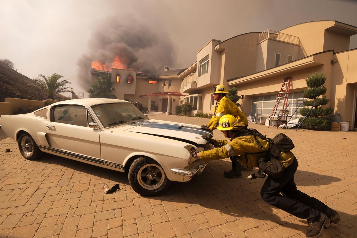 Firefighters push a vehicle from a garage as the Woolsy fire burning a home near Malibu Lake in Malibu, Calif., Friday, Nov. 9, 2018. About two-thirds of the city of Malibu was ordered evacuated early Friday as a ferocious wildfire roared toward the beachside community that is home to about 13,000 residents, some of them Hollywood celebrities. (Ringo H.W. Chiu / Associated Press)