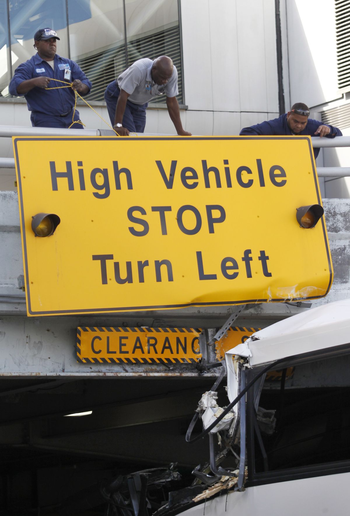Airport workers secure a sign after a bus hit a concrete overpass at Miami International Airport in Miami on Saturday, Dec. 1, 2012. The vehicle was too tall for the 8-foot-6-inch entrance to the arrivals area, and buses are supposed to go through the departures area which has a higher ceiling, according to an airport spokesperson. (Wilfredo Lee / Associated Press)