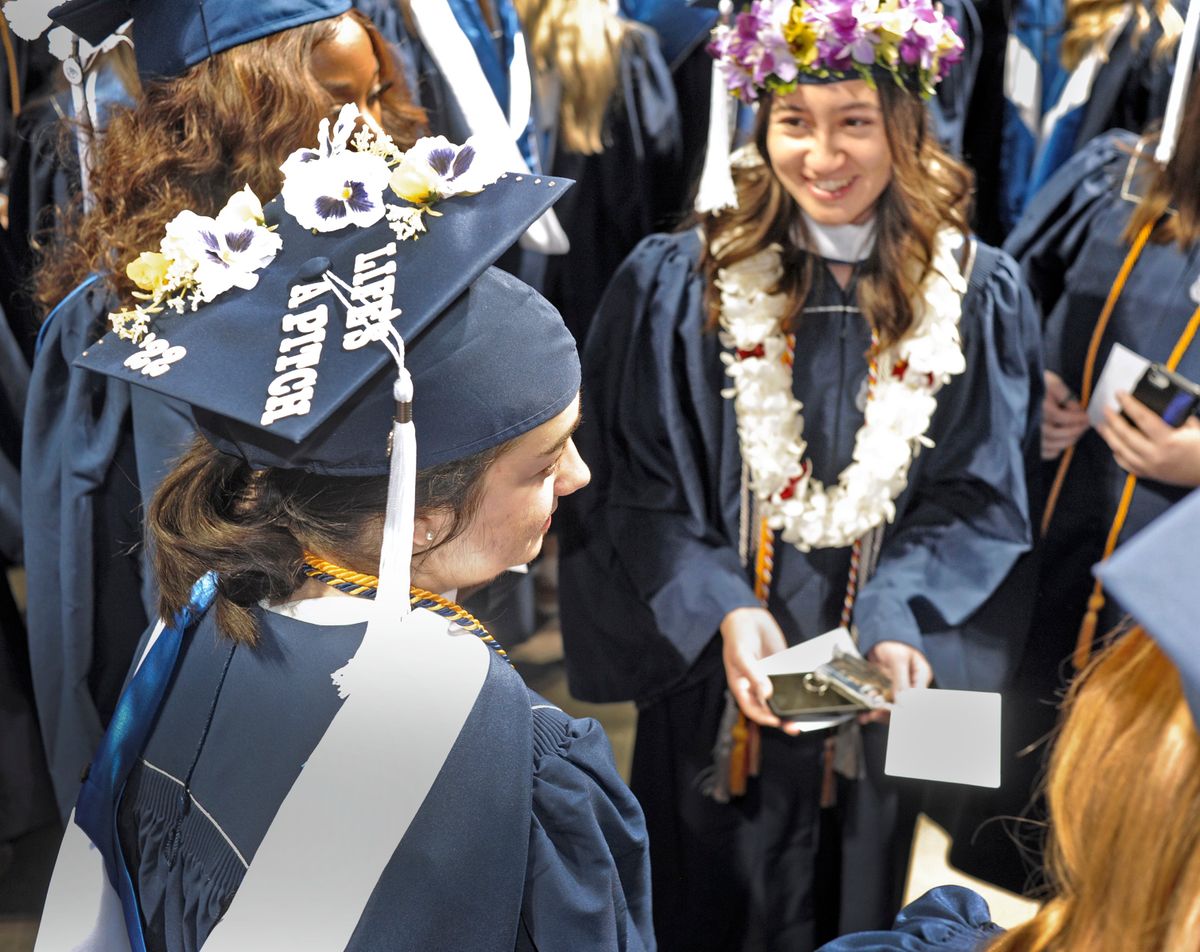 Sydney Bernardo, front left, sports a public relations message on the top of her mortarboard before graduation at the Spokane Veteran